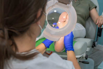 Female chiropodist, attending elder in a clinic and performing podiatric treatments