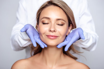 Close up portrait of young blonde woman with cosmetologyst hands in a gloves.